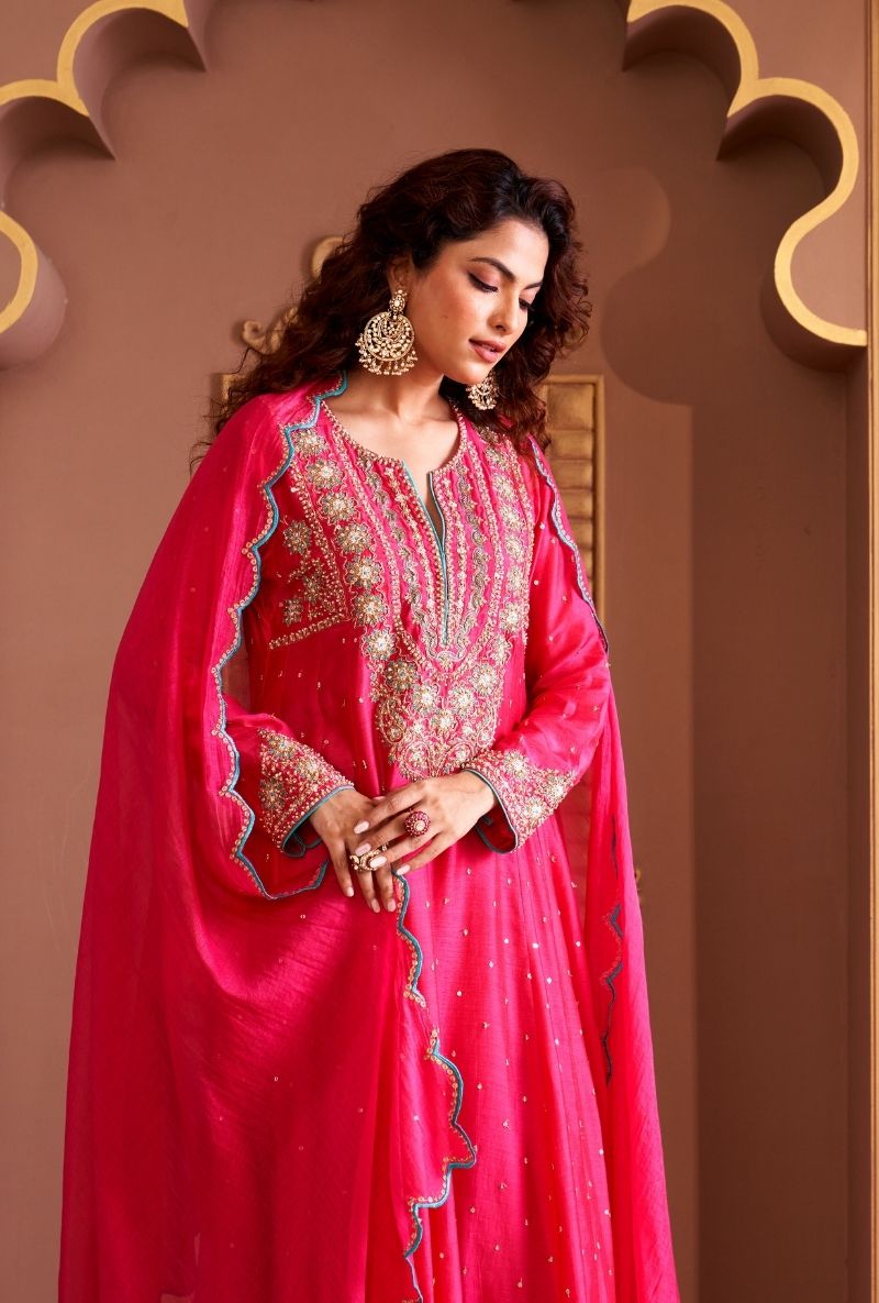 Woman in a pink traditional outfit with intricate designs against a decorative brown background