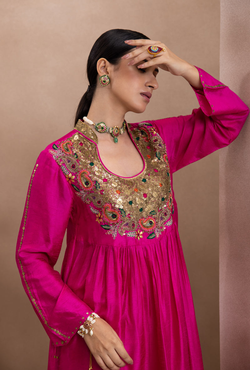 A woman wearing a pink kurta set with detailed embroidery and matching lower with tikki work.