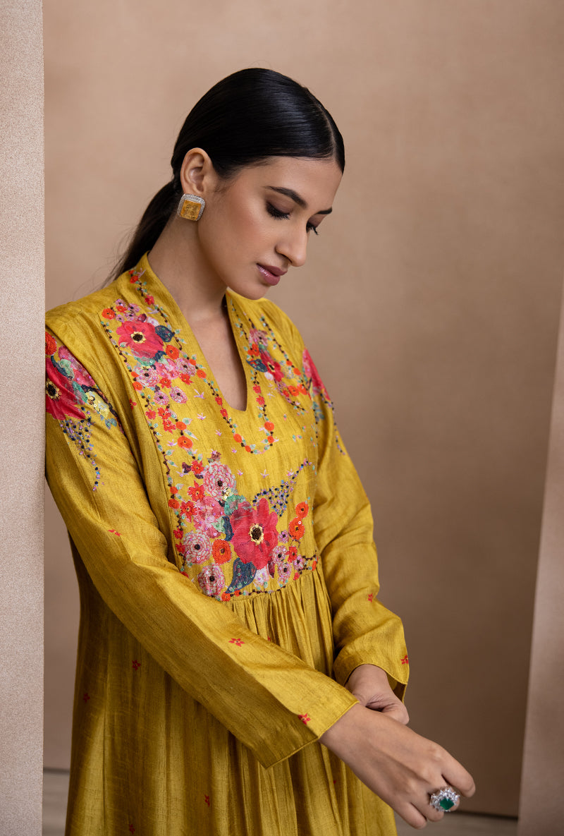 A woman wearing a yellow kurta set with front pleat and floral print, paired with a coordinating dupatta.