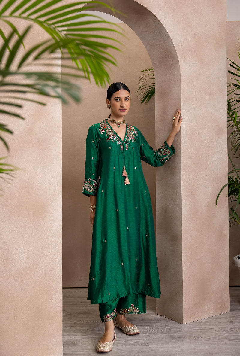 A woman wearing a green V-neck kurta set with paisley patterns and embroidery on the neck and cuffs, paired with dupatta.