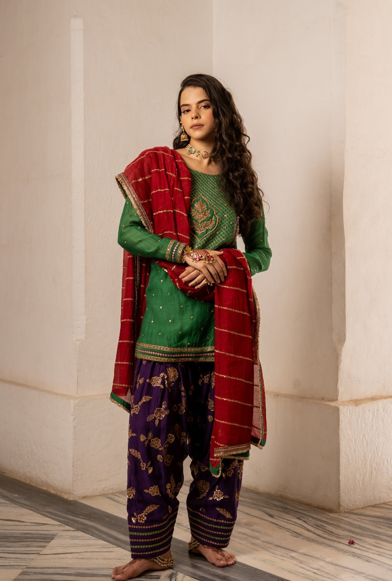 Woman in traditional green and purple outfit with red shawl indoors