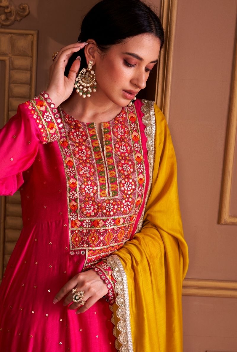 Woman wearing a traditional outfit with intricate embroidery in a warm-toned room.