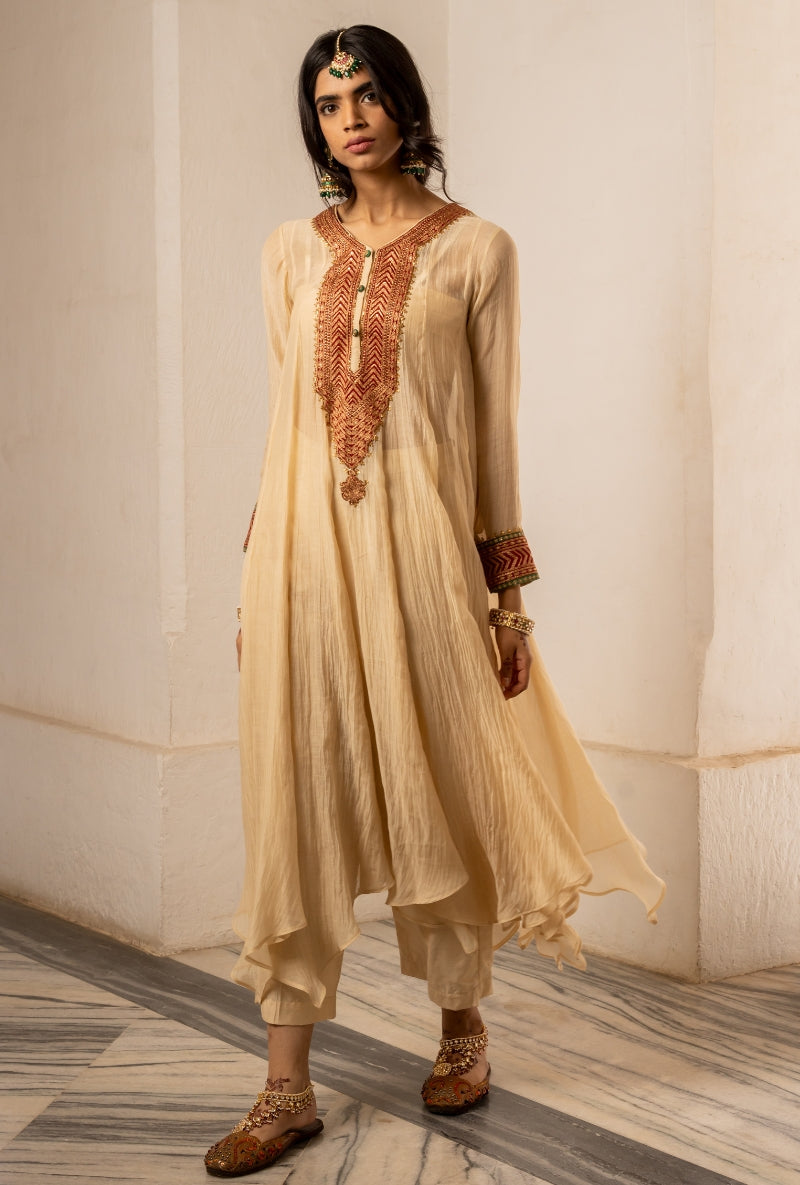 Woman wearing a beige traditional outfit with intricate embroidery in a neutral setting