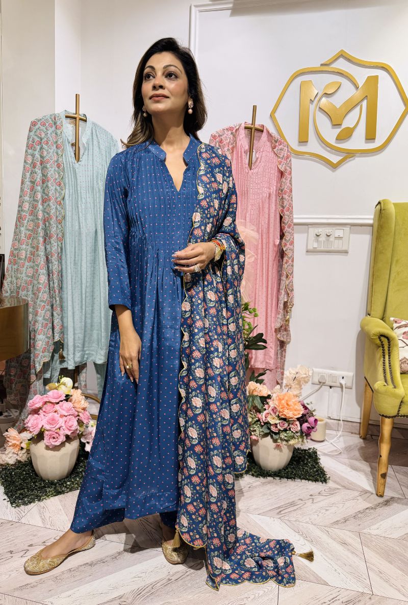 Woman in a blue and floral dress standing in a decorated room with flowers and furniture.