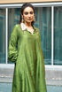 A woman wearing a green pankh collar adhira kurta set with leaf patterns and tikki embellishments, standing near a window.